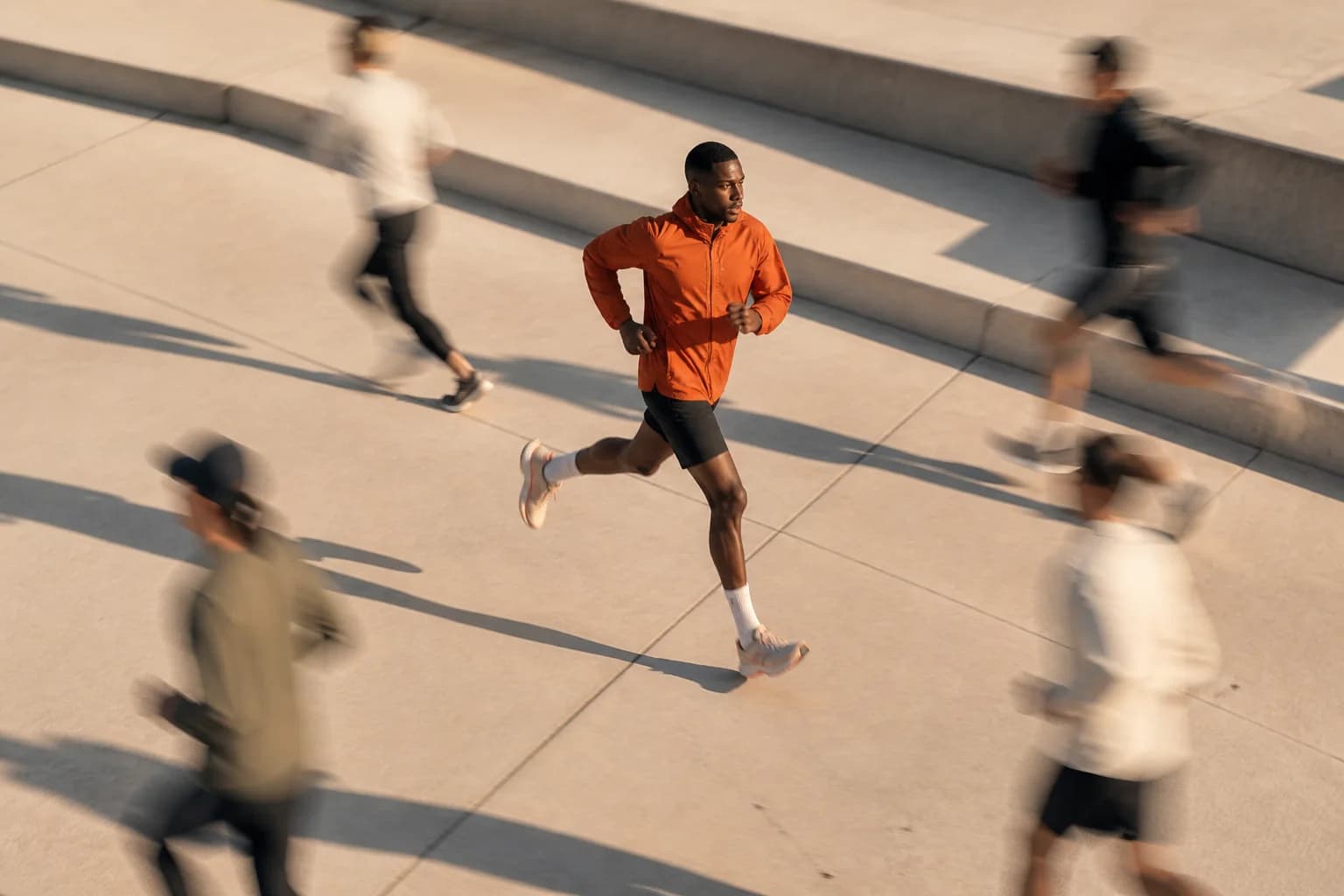 A runner in orange held sharply in view as surrounding athletes blur through a sunlit plaza