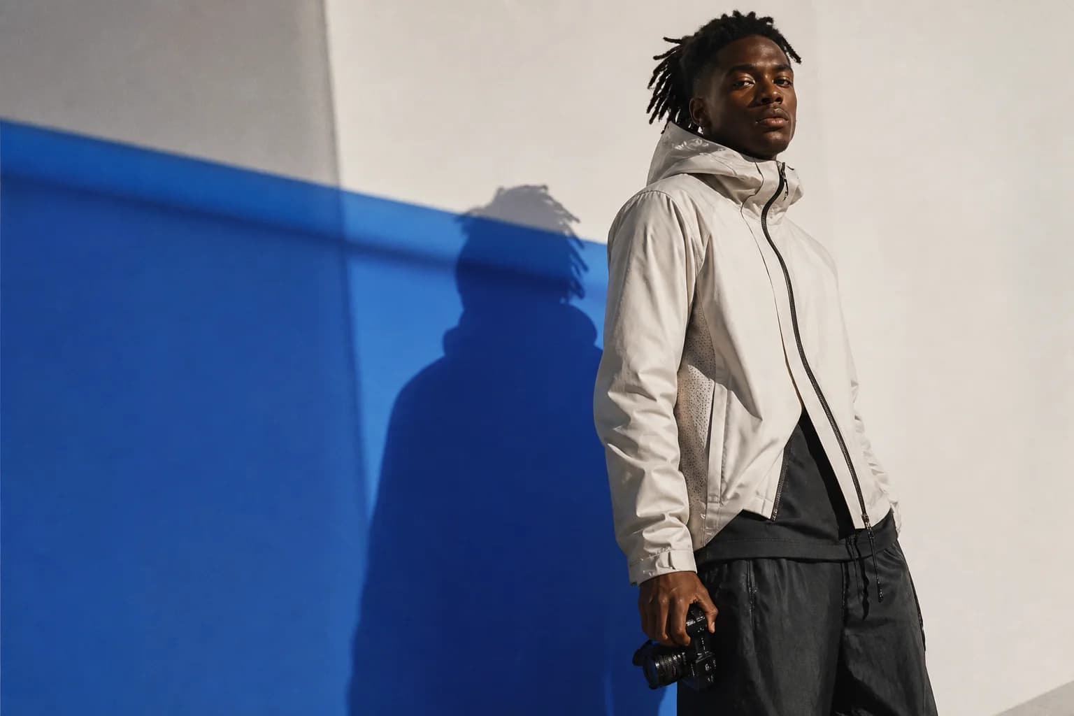 An athlete and creator in technical clothing standing against a cobalt studio shadow