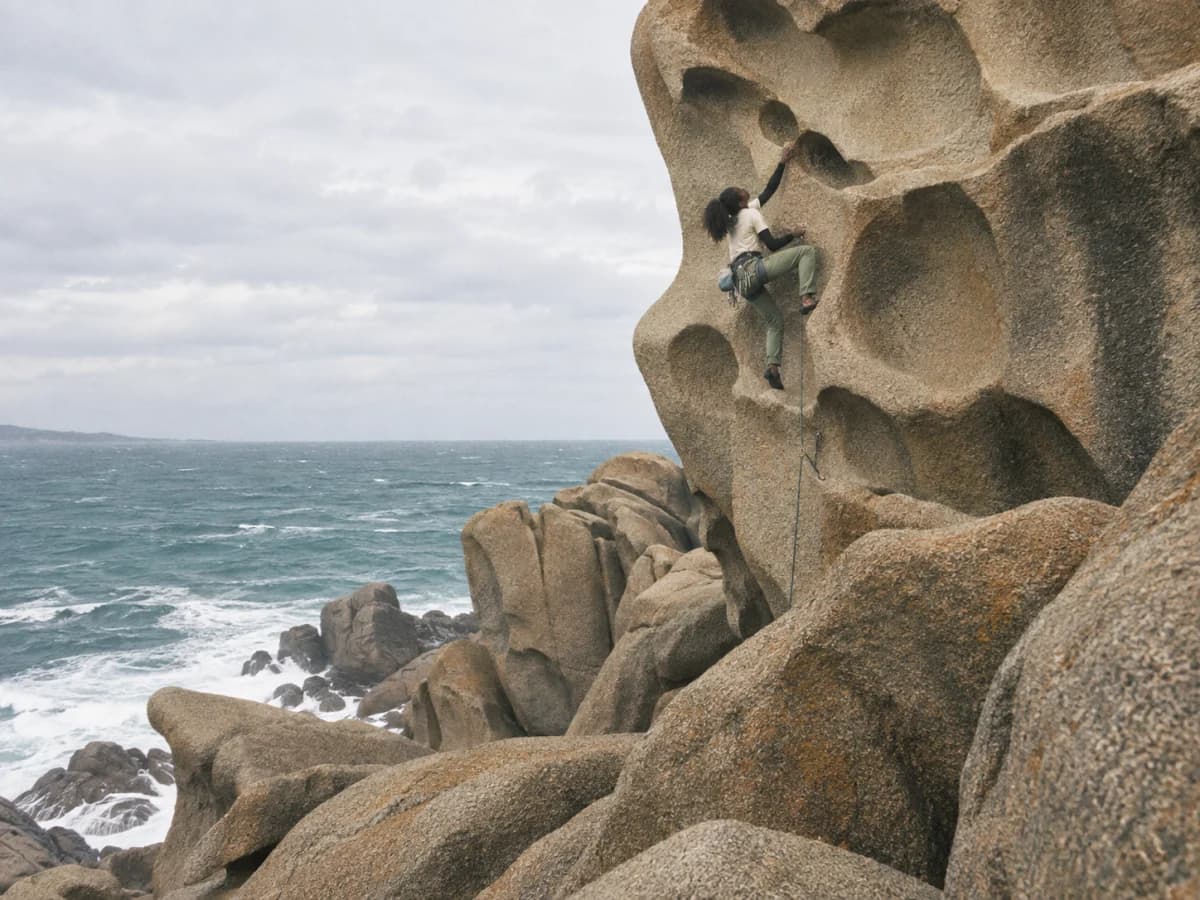 A climber scaling monumental coastal granite above the sea