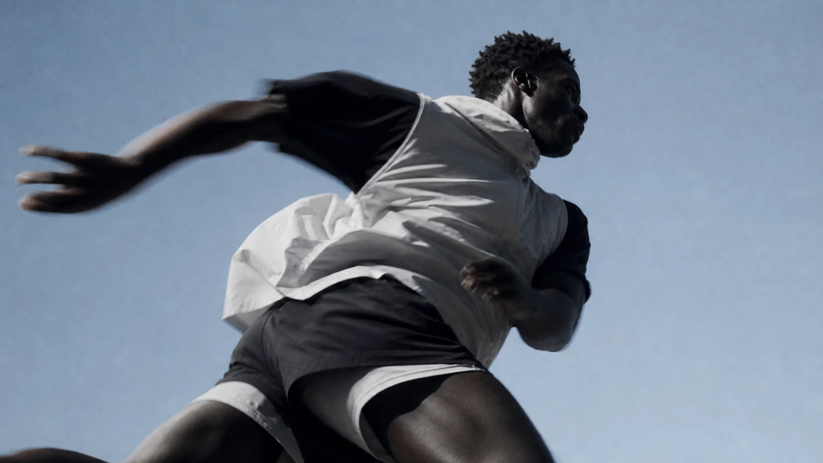 An athlete in a white vest photographed from below against the sky