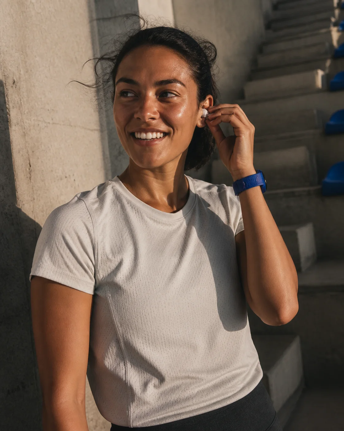 A runner smiling as she adjusts an earbud beside concrete stadium steps